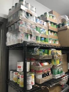 Metallic cans of tomatoes, corn, and other foods all stacked upon a shelf