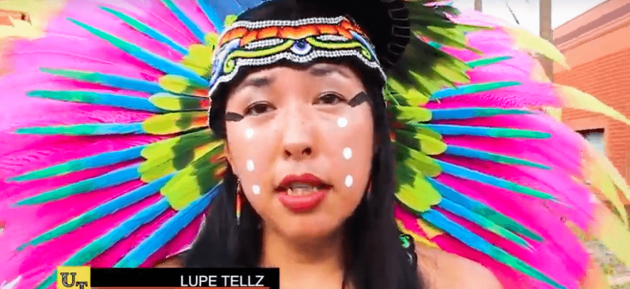 Lupe+Tellz+is+wearing+a+flamboyant+pink%2C+lime+green%2C+and+yellow+feather+on+the+top+of+her+head