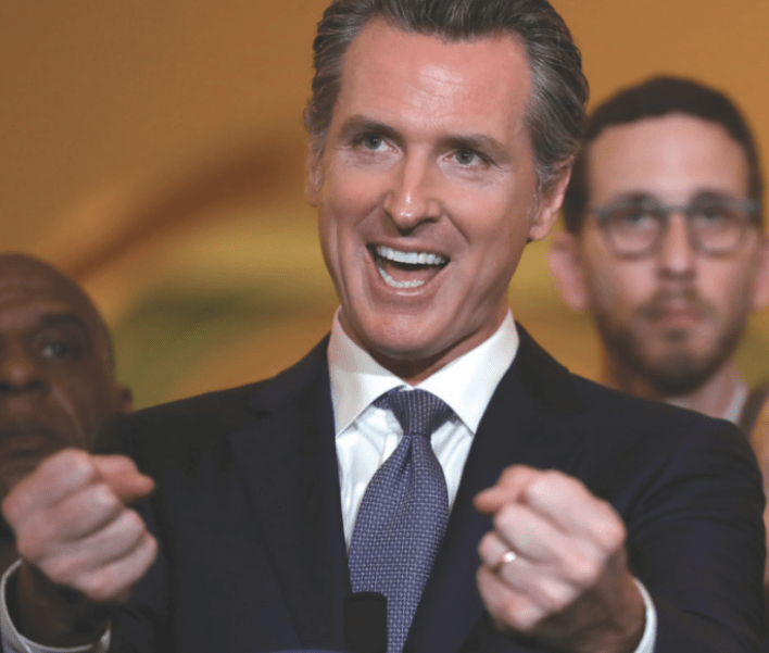 Governor of California, Gavin Newsom, is smiling in this picture with his hands in a fist motion.