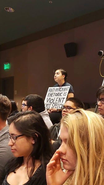 A girl is holding up a sign which says Anti-Immigrant Rhetoric is Violent: Free Speech