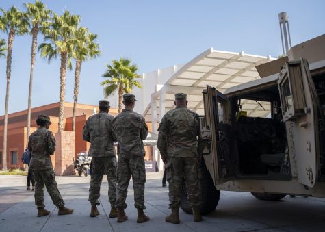 People in uniform stand side-by-side each other next to the parked Humvees.