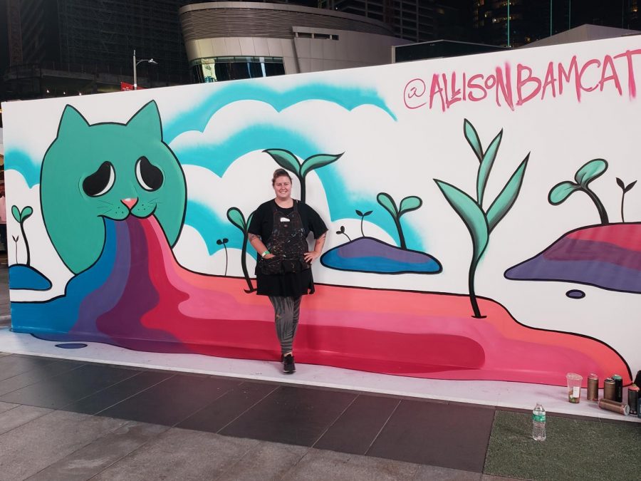 Allison BamCat posing in front of her Too Much Fun mural. (Amairani Hernandez/UT)