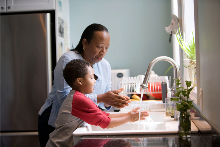 A mother teaches her son how to properly wash his hands at their kitchen sink. She has him briskly rub his soapy hands together under fresh running tap water, to remove contaminants, which reduces the spread of pathogens. (Photo courtesy of the CDC)