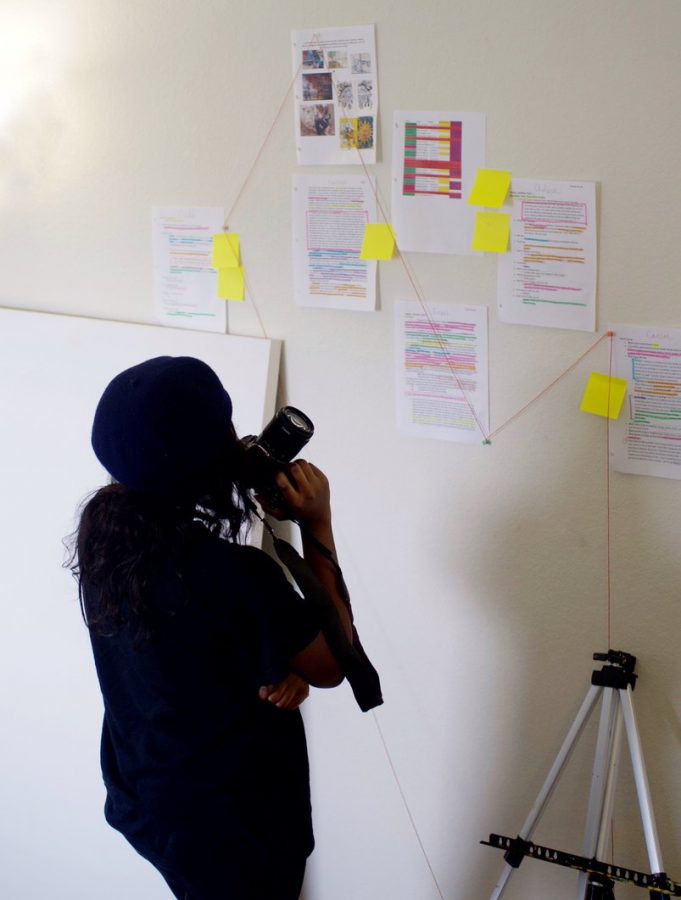 Maryse Bombito looks at papers with notes taped to a wall as she organizes her Healing Through Art project.
