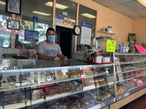Arturo Nunez, a small business owner, stands behind the counter at his shop while wearing a mask.
