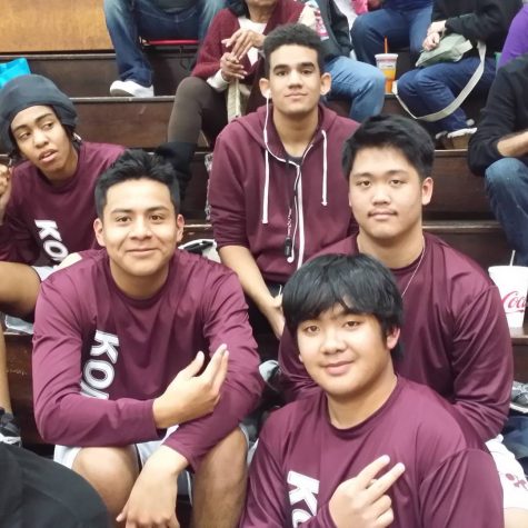 Jericho Dancel and his wrestling teammates sit on some bleachers wearing maroon uniforms.