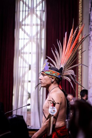 Man with armband and headress with orange and brown feathers