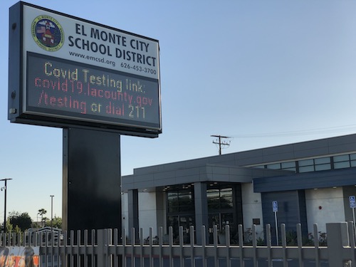 An electronic sign with a school building behind it