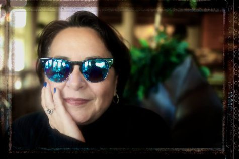 A woman smiling and wearing sunglasses, resting her chin on her hand