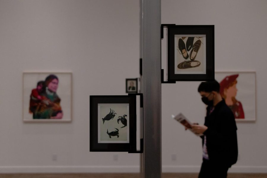 Photos shows a student walking by two framed pictures, one of two pairs of shoes and the other of crabs. 