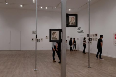 Photo shows people in the gallery and the focus is on two framed polaroids stuck to a pole. 