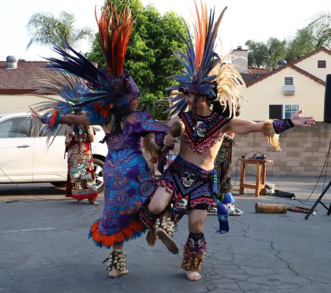 Two people in traditional clothes and colorful feather headdresses dance.