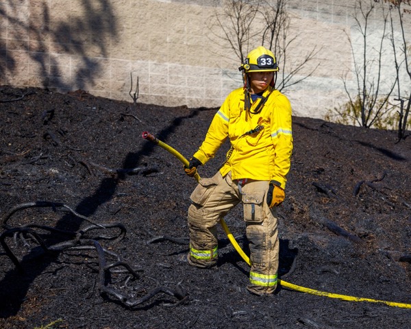 Man in yellow uniform and hat holds black hose