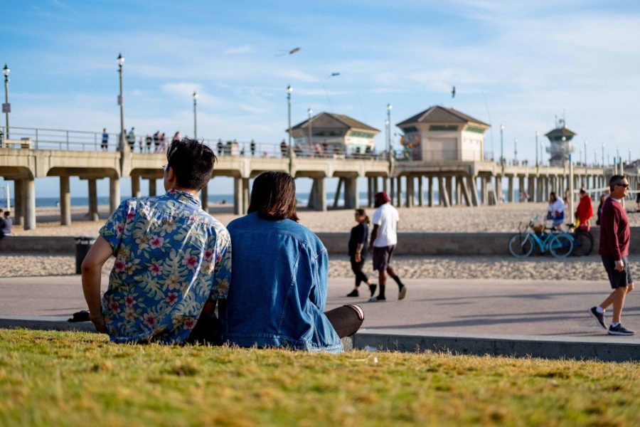 A couple sitting on the grass by a pier.