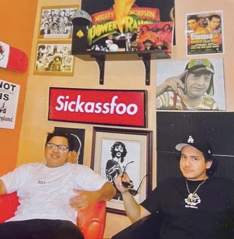 Two guys sitting in front of an orange wall full of colorful posters