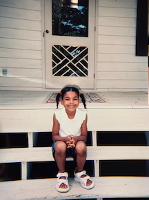 A young Alyssah sitting in the steps of her house 