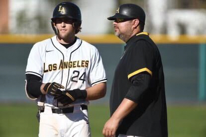 A baseball player in uniform talking to his coach during a game.
