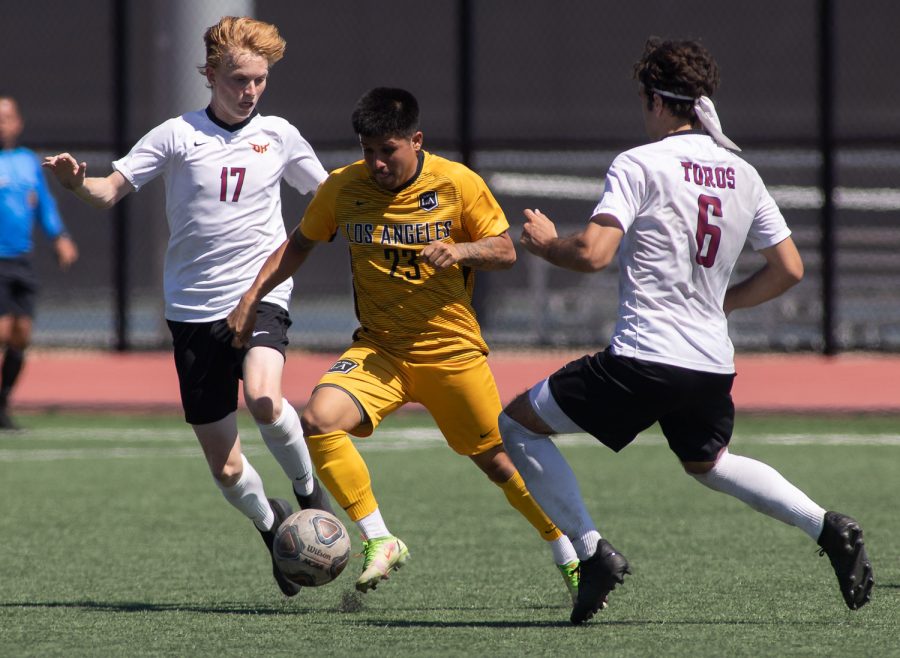 Cal State LA Soccer player dribbles against two Dominguez Hills players.