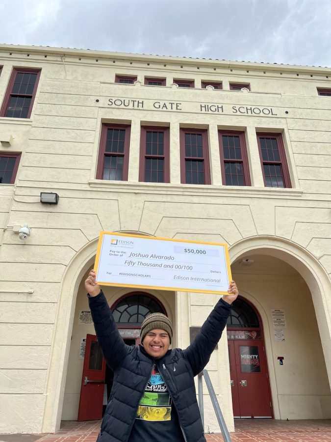 Joshua Alvarado in front of his high school holding a check for $50,000.