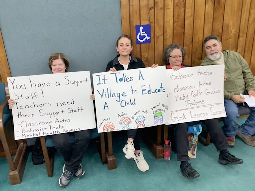 A group of people/teachers holding signs protesting against district layoffs.