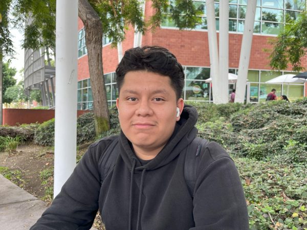A photo of a college student with an airpod in his left ear and a black hoodie on.