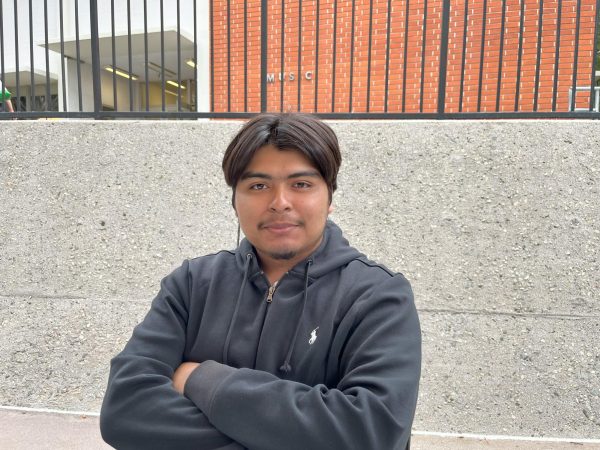 A photo of a college student with his arms crossed and a blueish grey jacket on.