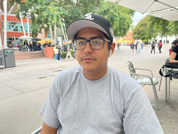 A photo of a college student with a black cap, grey shirt, and glasses on.