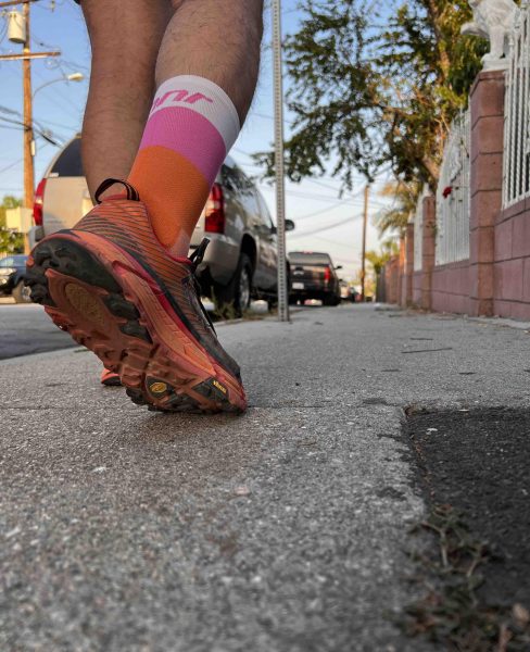 White, pink and orange socks on a running with a one foot on the pavement and one up. 