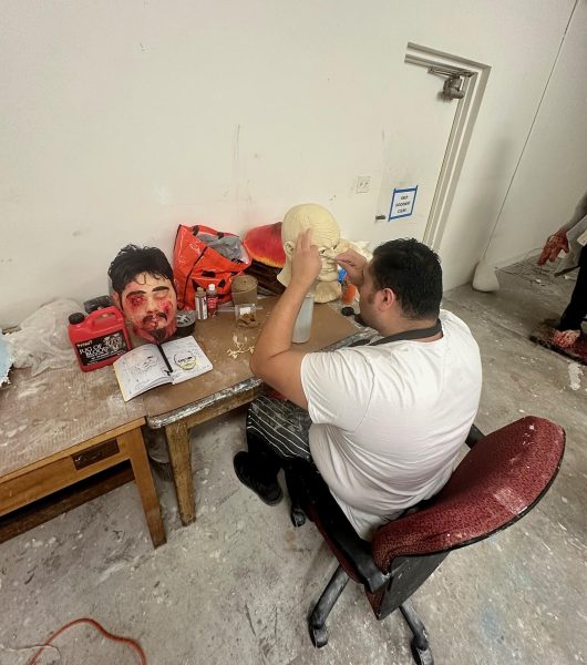 Carlos sitting at a table working on sculpting a mask. 