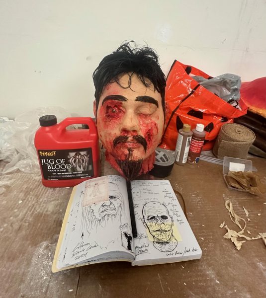 A sculpted replica of Carlos' severed head sitting on a table with his sketchbook. 