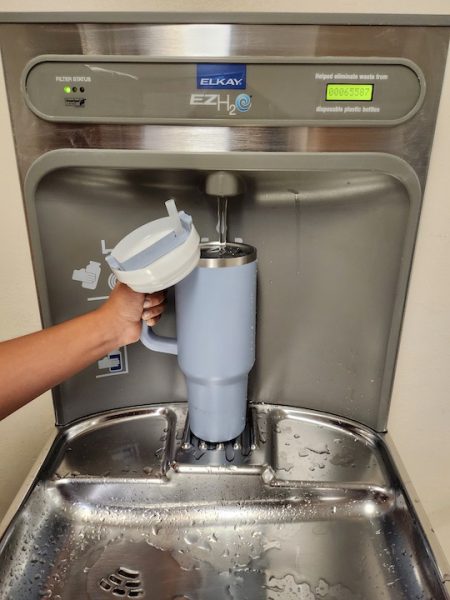 A blue HydroFlask being refilled at a water fountain.