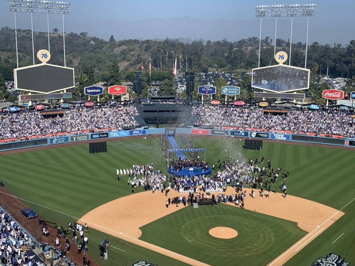 Dodger fans and players celebrate at rally as confetti falls on the field.