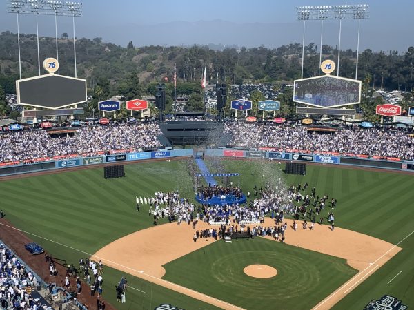 Dodger fans and players celebrate at rally as confetti falls on the field.