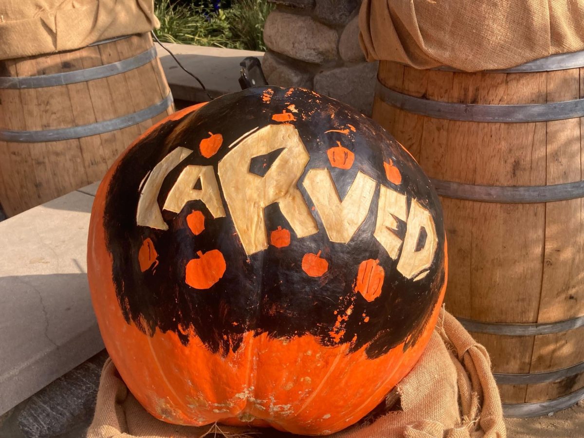 A pumpkin on top of a burlap sack on a barrel that bears the logo for "Carved."