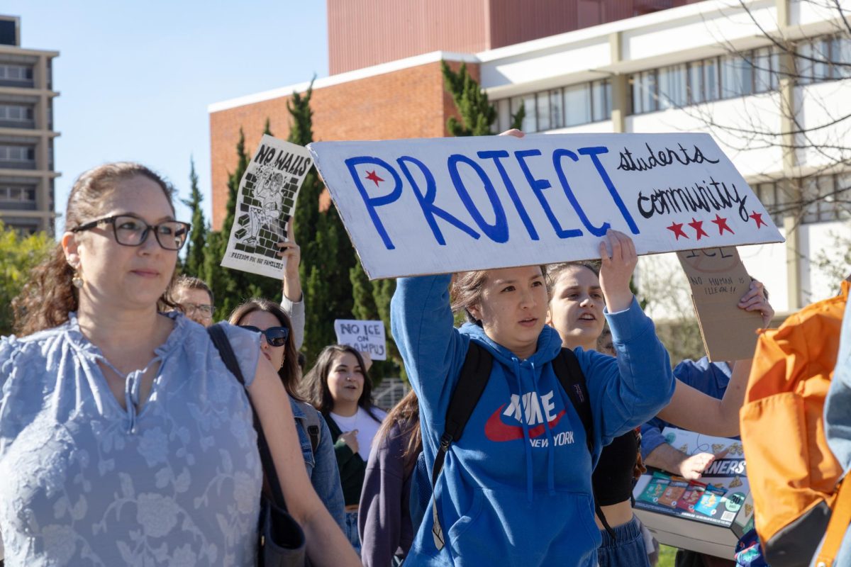 Grace Park, a second year student in the social work masters program, holds a sign and leads a protest of about 30 participants through the university's main walkway on Tuesday Jan. 20, 2026
