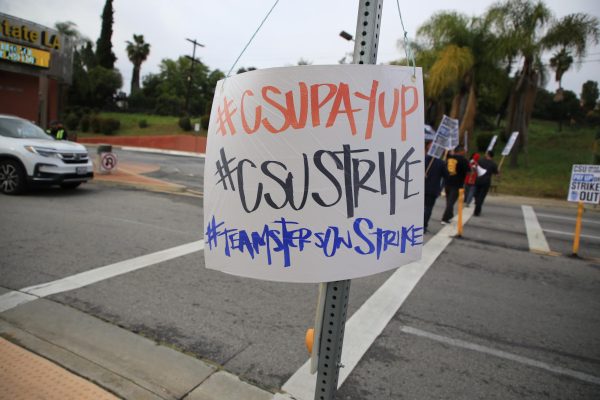 A protest sign hangs on a road sign made by the Teamsters at the Cal State LA Welcome Center Picket Line.