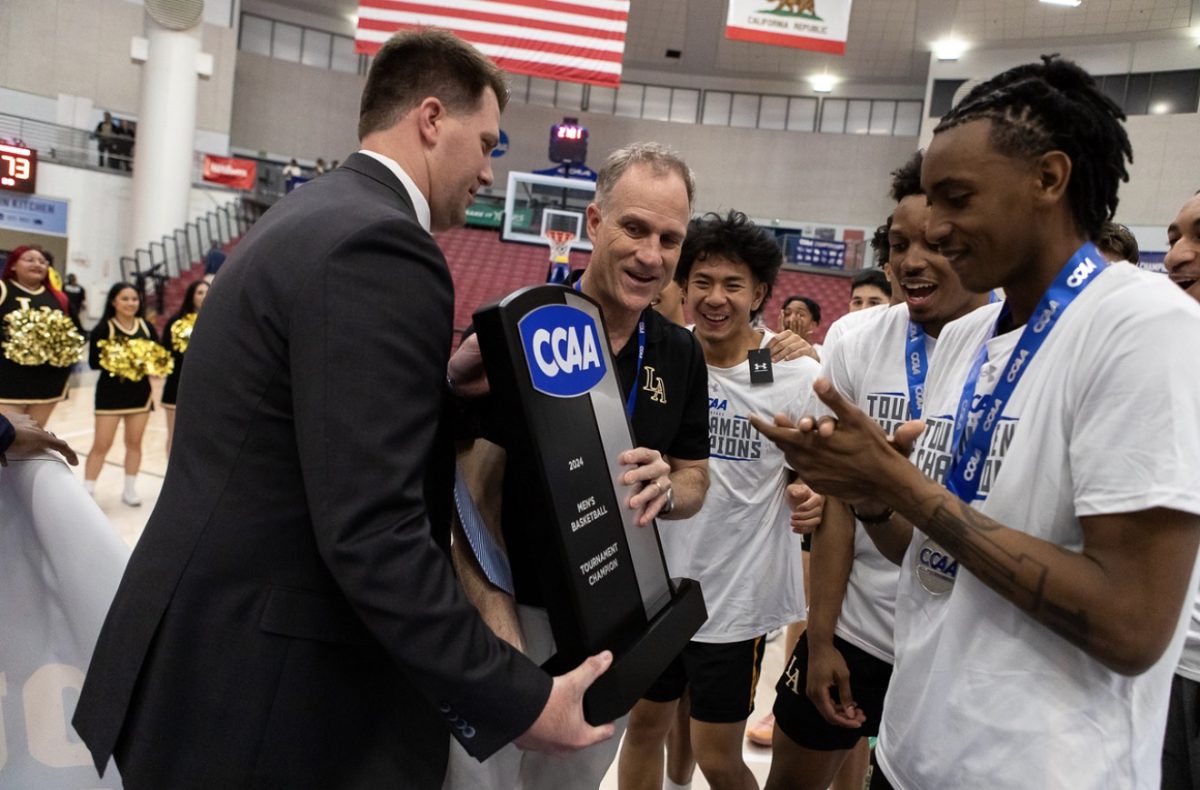 Head Coach Jim Saia accepts the CCAA championship trophy as members of the Cal State LA men’s basketball team gather around him in celebration following the 2024 season’s title victory.
Surrounded by players, Saia holds the trophy, marking a milestone achievement for the Golden Eagles program. Photo courtesy of Will G. MacNeil